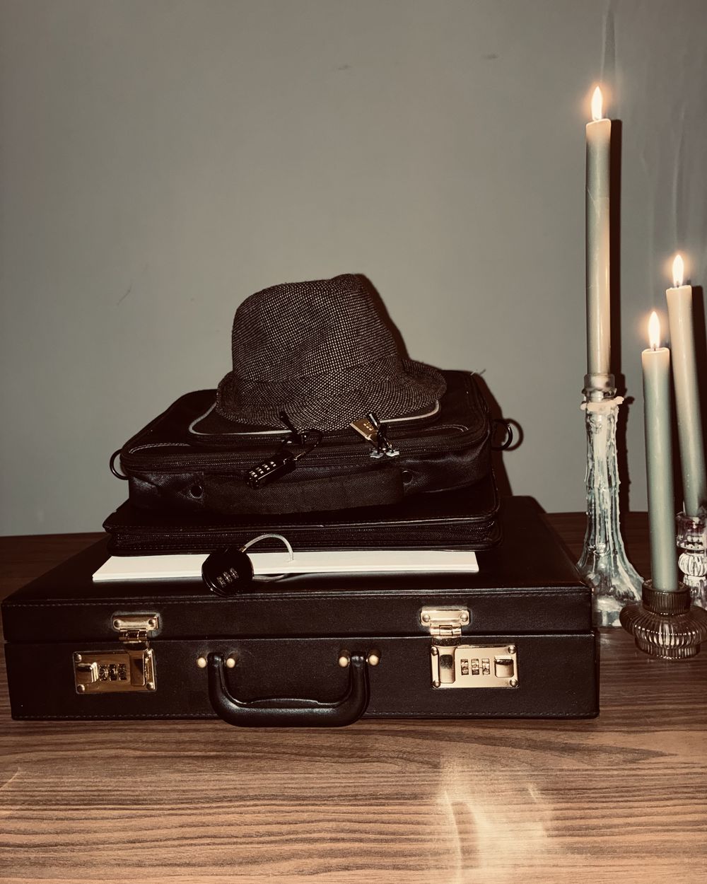 A stack of briefcases with a hat, next to burning candles